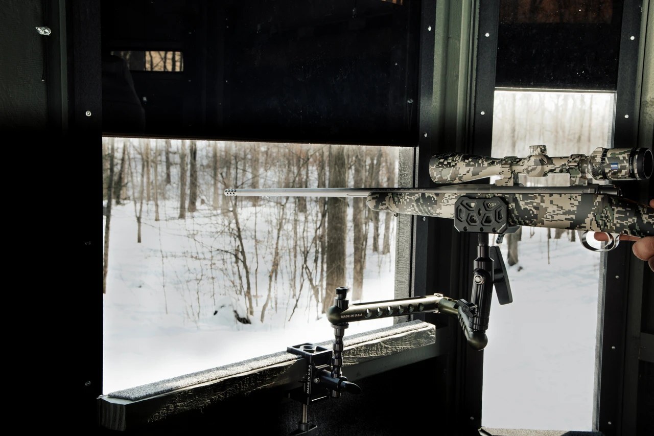 A rifle held steady at the window of a box blind, with nothing standing on the floor.